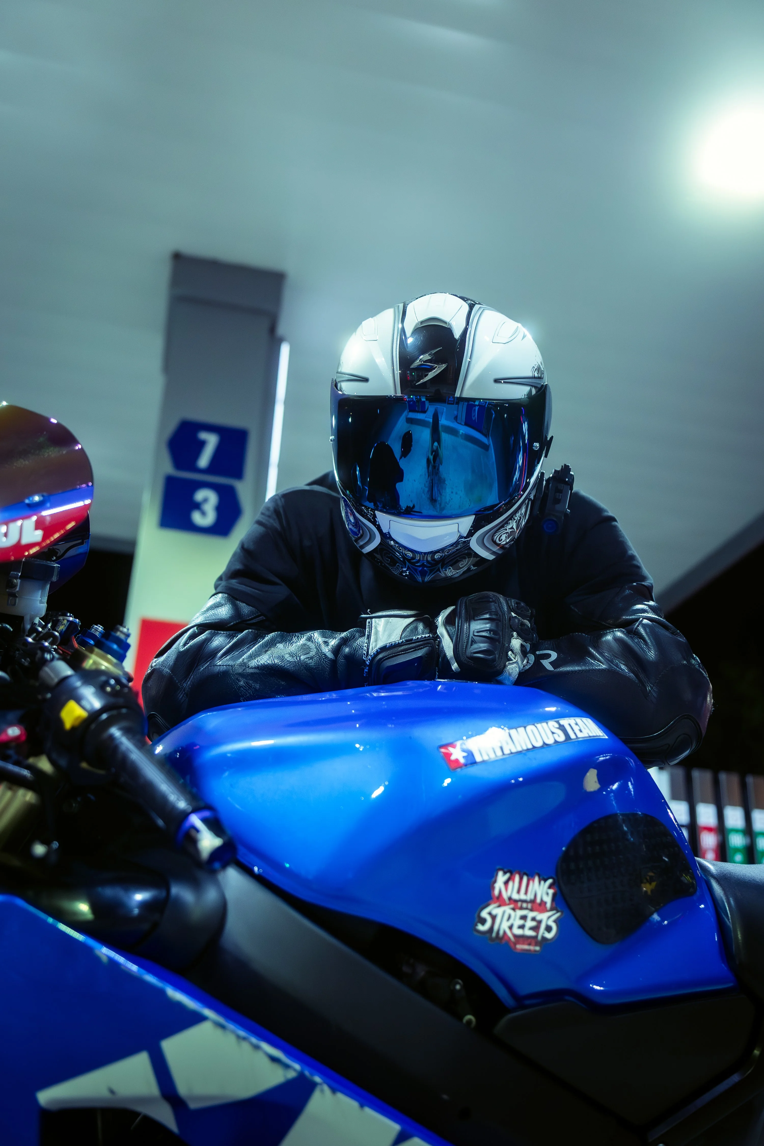 Motocyklista na niebieskim motocyklu na stacji benzynowej nocą