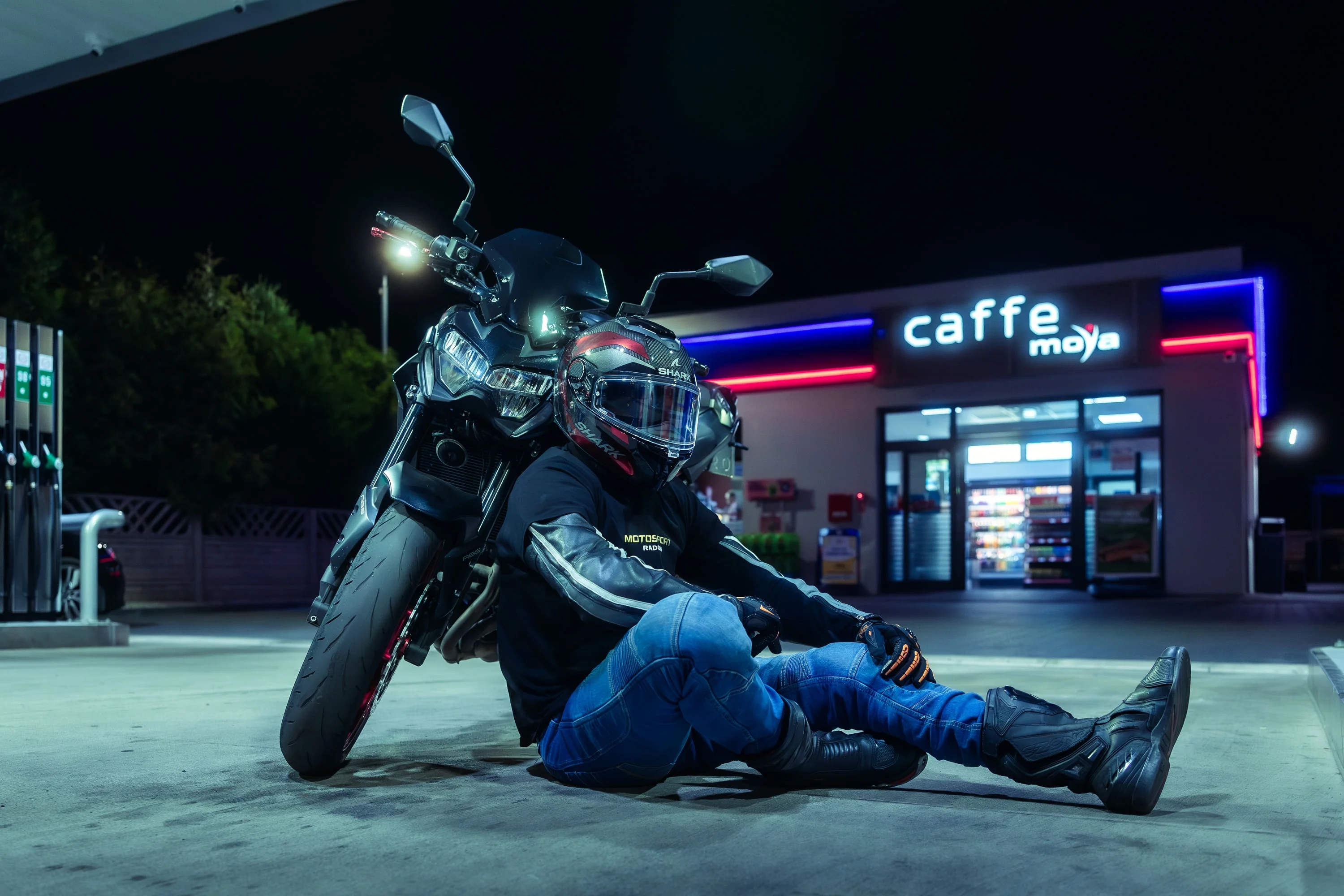 Motocyklista oparty o motocykl na stacji benzynowej nocą